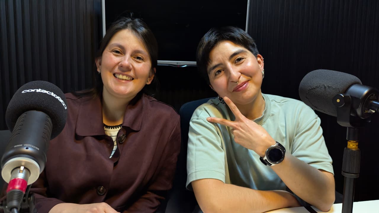 Marcela Sanhueza y Águe sonríen junto a dos micrófonos en un estudio de radio.