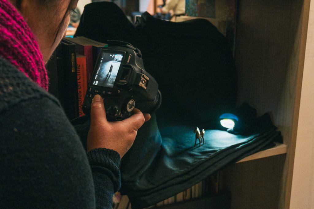 Una persona fotografía una figura en miniatura iluminada por una linterna sobre una tela negra.