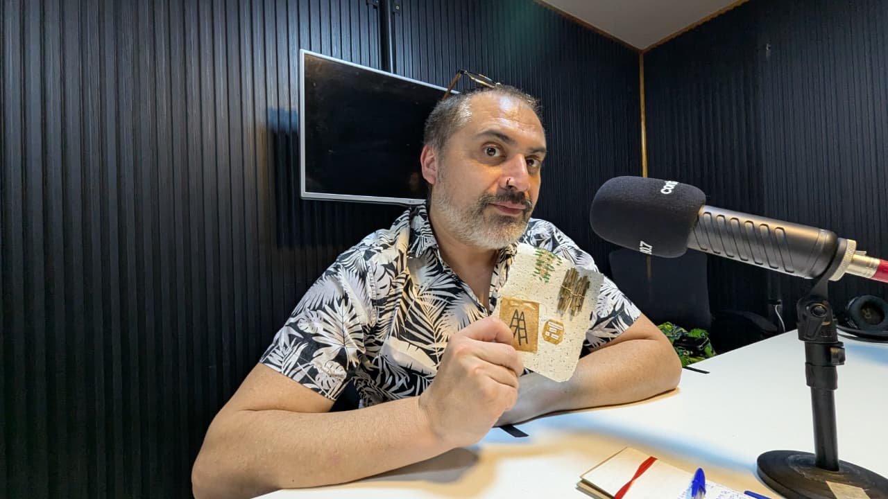 Sergio Cofré sentado frente a un micrófono en un estudio de radio, con una camisa de estampado vegetal.
