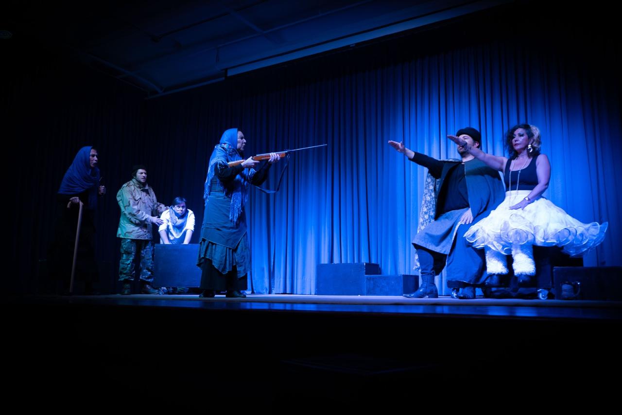 Intérpretes de Una Tierra Partida durante una escena del montaje teatral en un escenario iluminado de azul.
