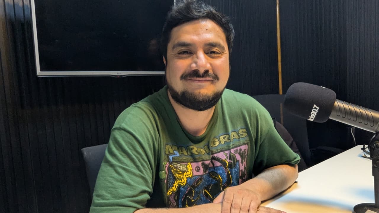 Víctor Sanhueza, con polera verde, sentado junto a un micrófono en un estudio de radio.